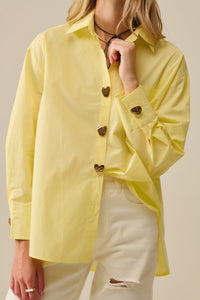 Person wearing a yellow shirt with heart-shaped buttons on a beige background