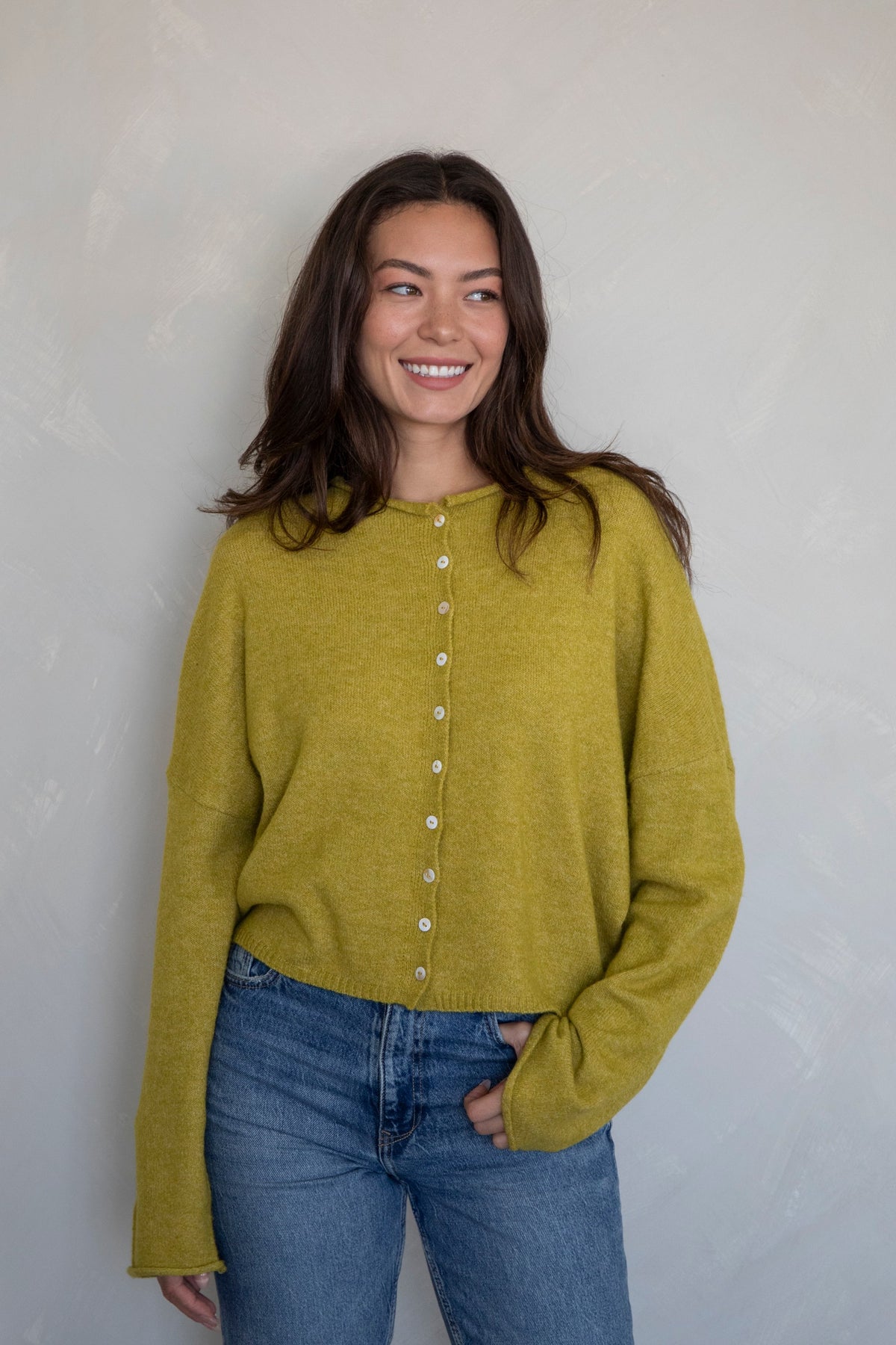 mustard yellow button-up cardigan on a girl in front of a white wall.