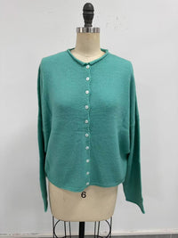 turquoise button-up cardigan on a mannequin in front of a white wall.