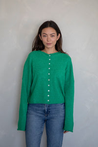 kelly green button-up cardigan on a girl in front of a white wall.