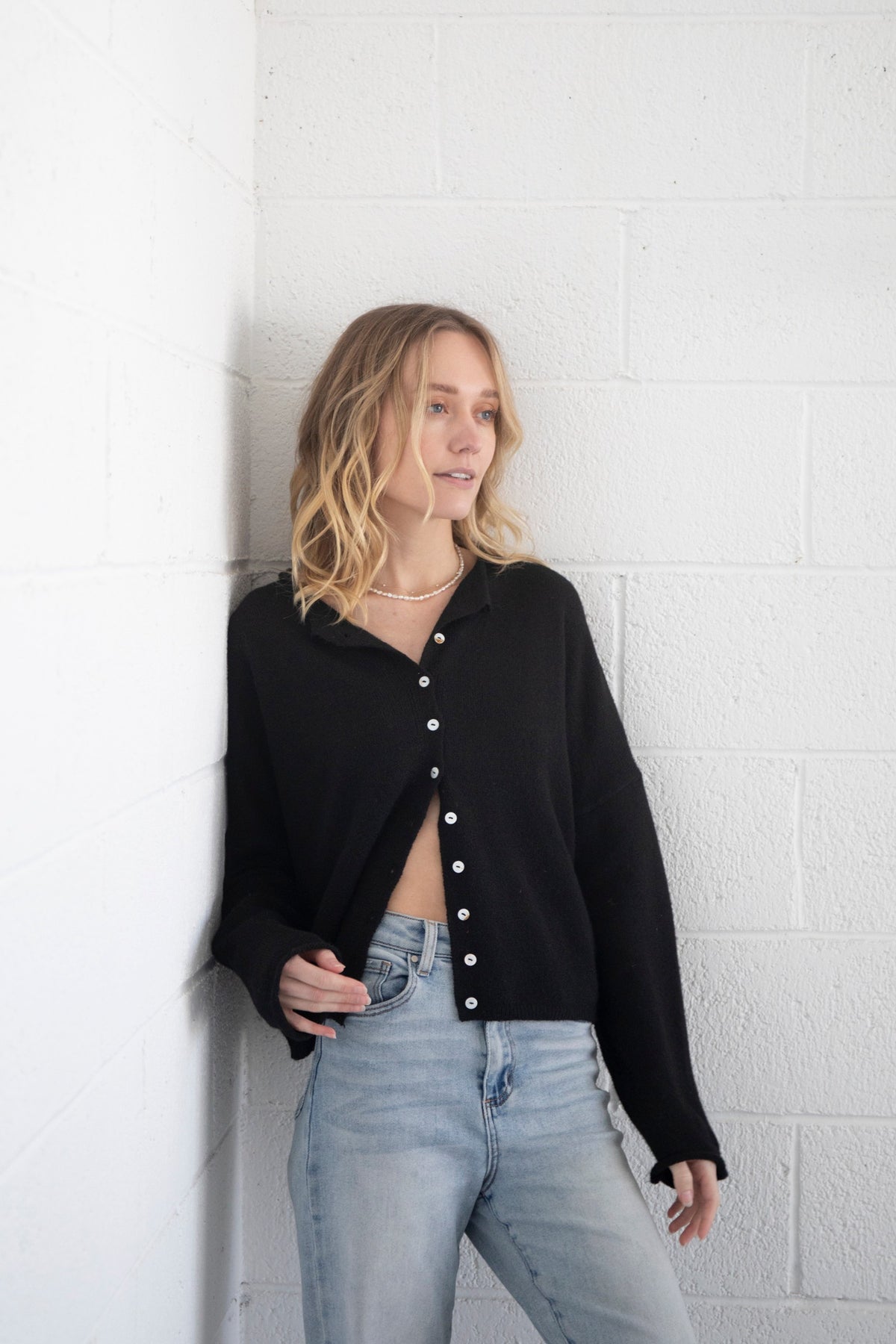 black button-up cardigan on a girl in front of a white wall.