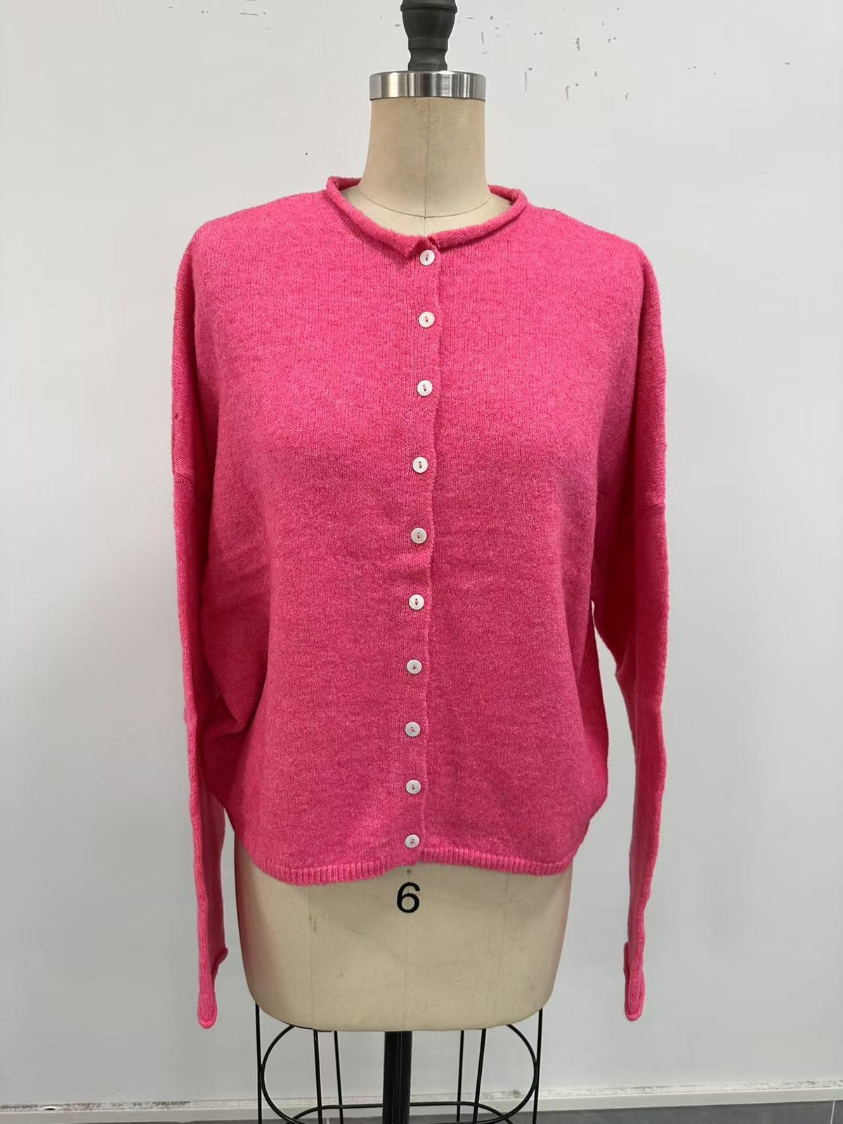 rose pink button-up cardigan on a mannequin in front of a white wall.