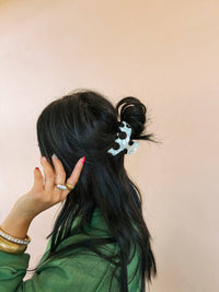 Person with a ponytail wearing a green jacket against a beige background