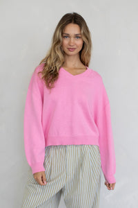 a girl wearing a bubblegum pink sweater & striped pants, standing in front of a white wall.