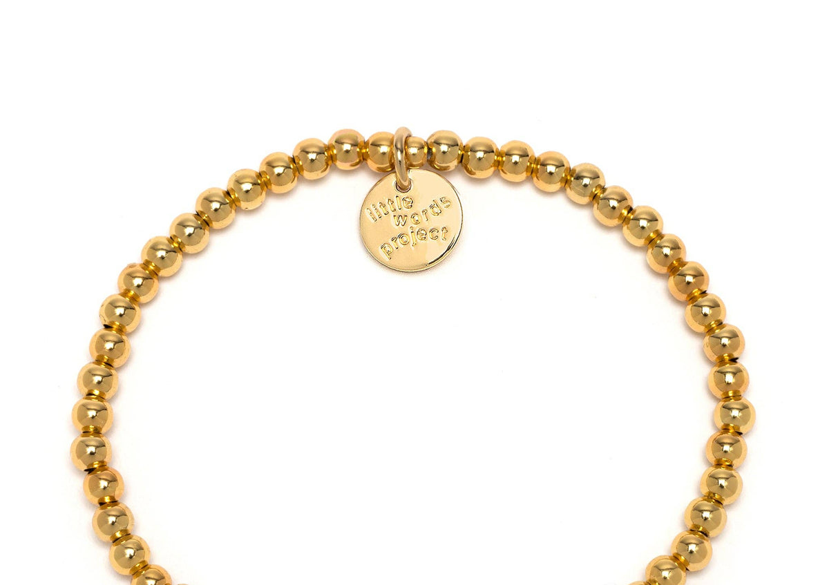 Gold beaded bracelet with a black and white 'YOUR TEXT' charm on a white background