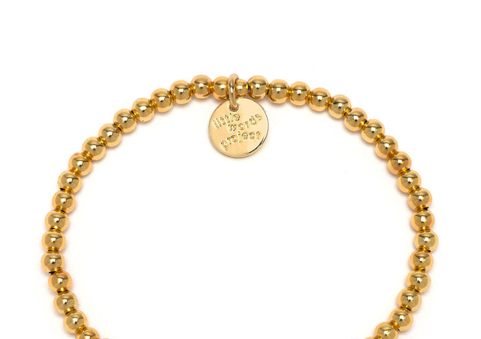 Gold beaded bracelet with a black and white 'YOUR TEXT' charm on a white background