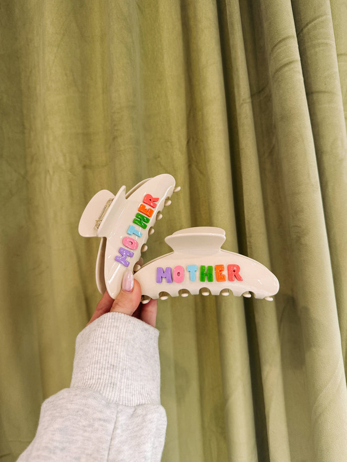 Hair clip with 'MOTHER' text held in front of a green curtain