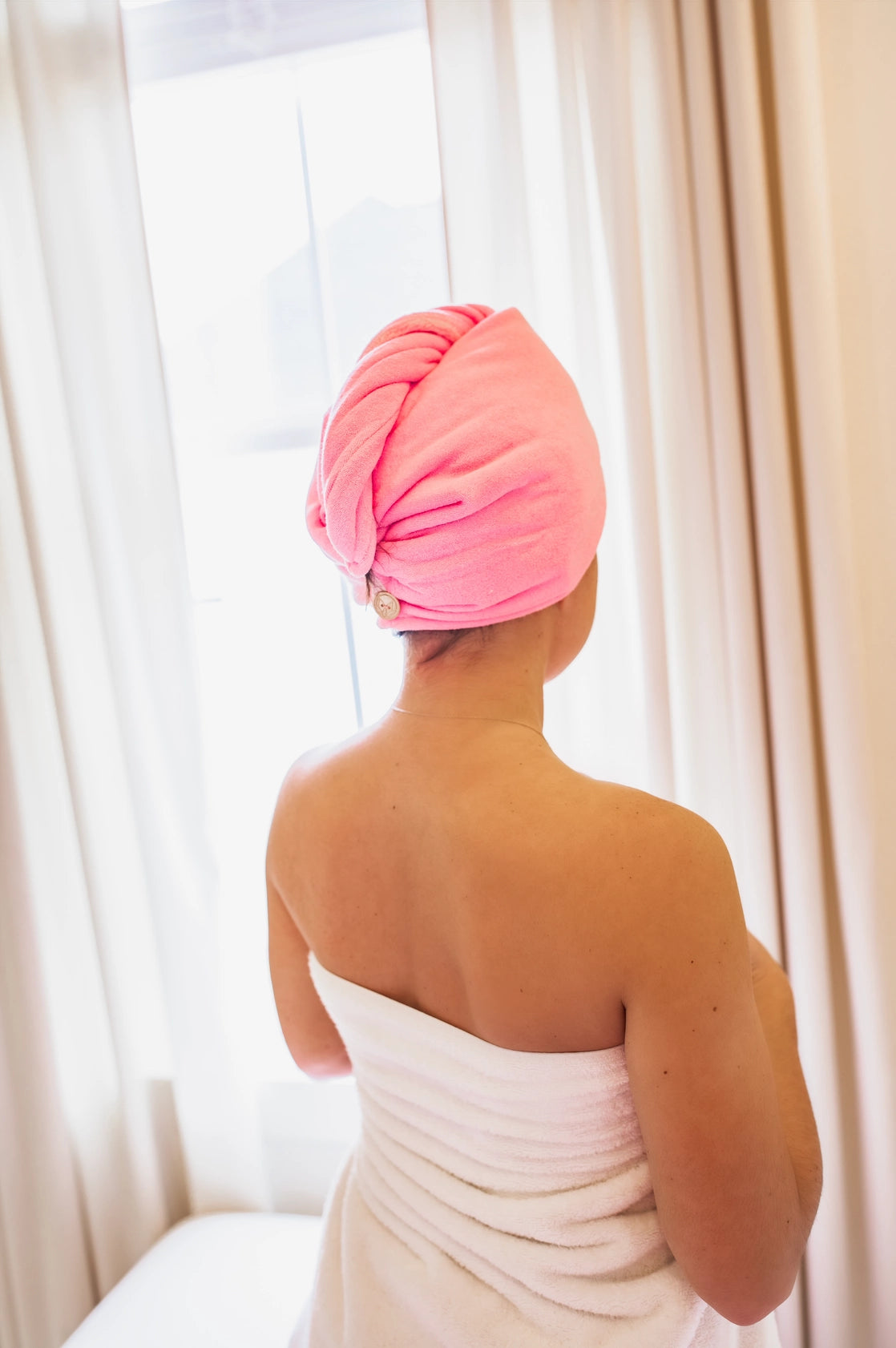 Person wearing a pink towel on their head with white curtains in the background