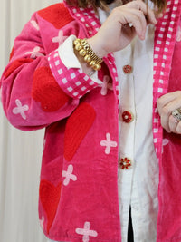 Close-up of a person wearing a pink jacket with red and white patterns on a neutral background