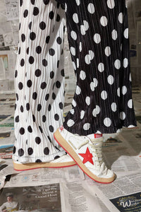 Person wearing black and white polka dot pants with a red star sneaker on a newspaper background