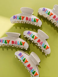 Set of white hair clips with colorful 'Dilly Dally' text on a green background