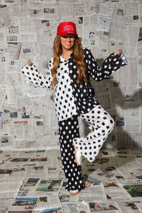 Person wearing a black and white polka dot outfit with a red cap in front of a newspaper wall.