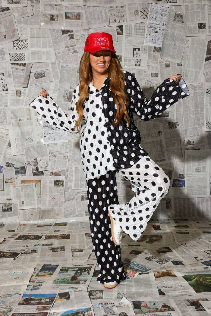 Person wearing a black and white polka dot outfit with a red cap in front of a newspaper wall.