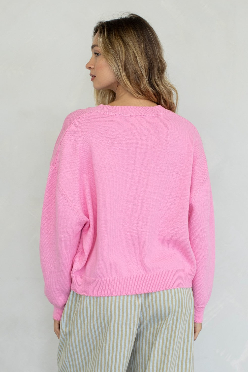 a girl wearing a bubblegum pink sweater & striped pants, standing in front of a white wall.