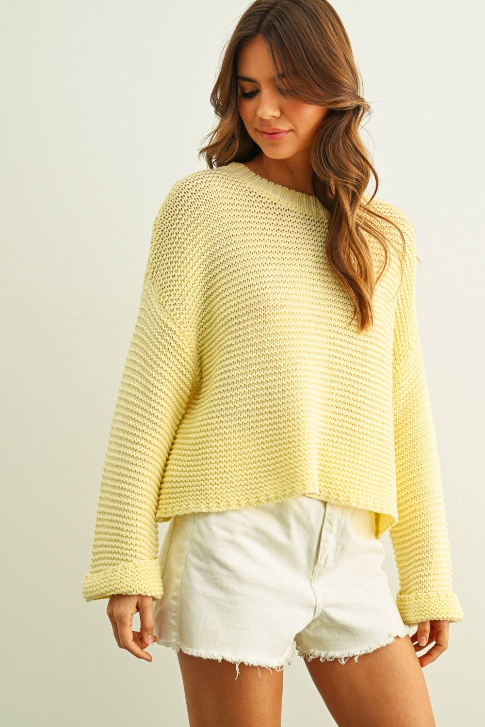 Woman wearing a light yellow knitted sweater and white shorts on a plain background