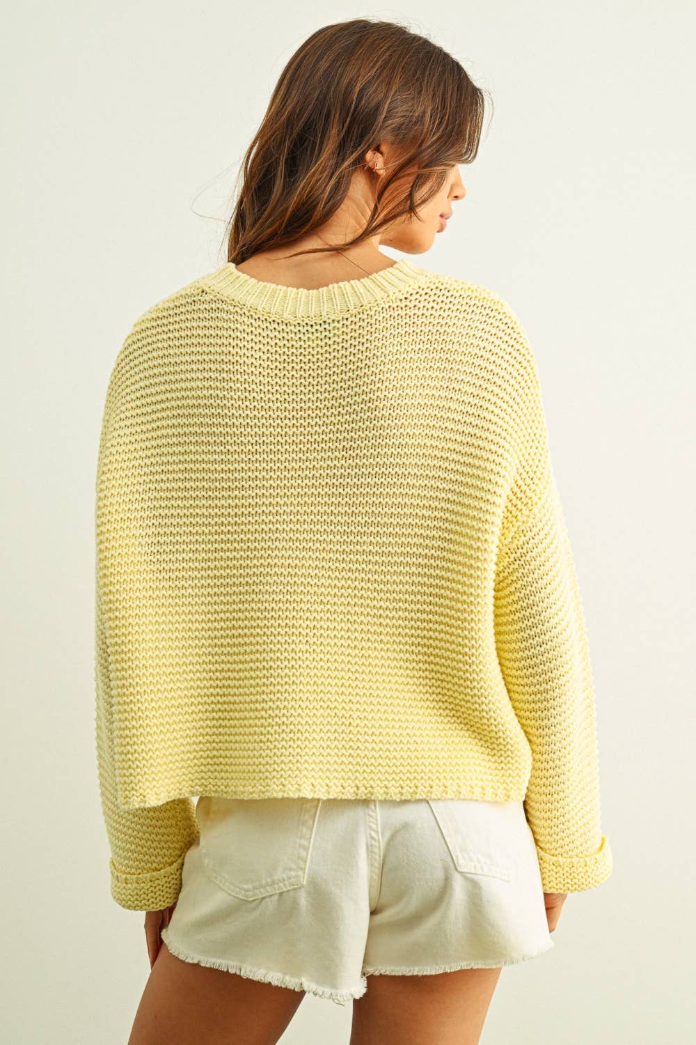 Woman wearing a yellow knitted sweater and white shorts on a plain background