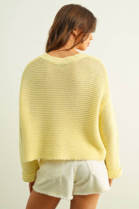 Woman wearing a yellow knitted sweater and white shorts on a plain background