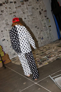 Person wearing a black and white polka dot outfit with a red cap, standing in a room with newspaper walls.