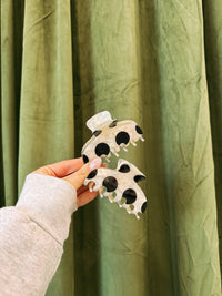 Hand holding a polka dot hair clip against a green curtain background