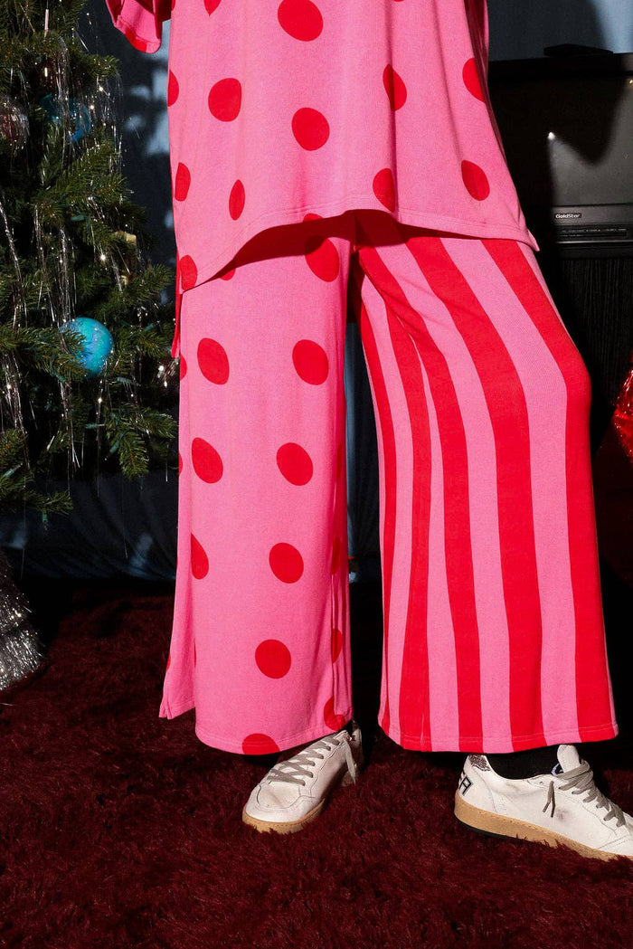 Person wearing pink pants with red polka dots and stripes, standing in front of a decorated Christmas tree.