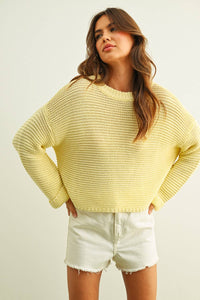 Woman wearing a yellow knitted sweater and white shorts on a plain background